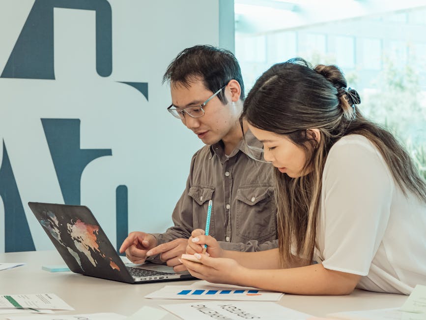 Two professionals engaged in a focused team meeting using a laptop and documents.